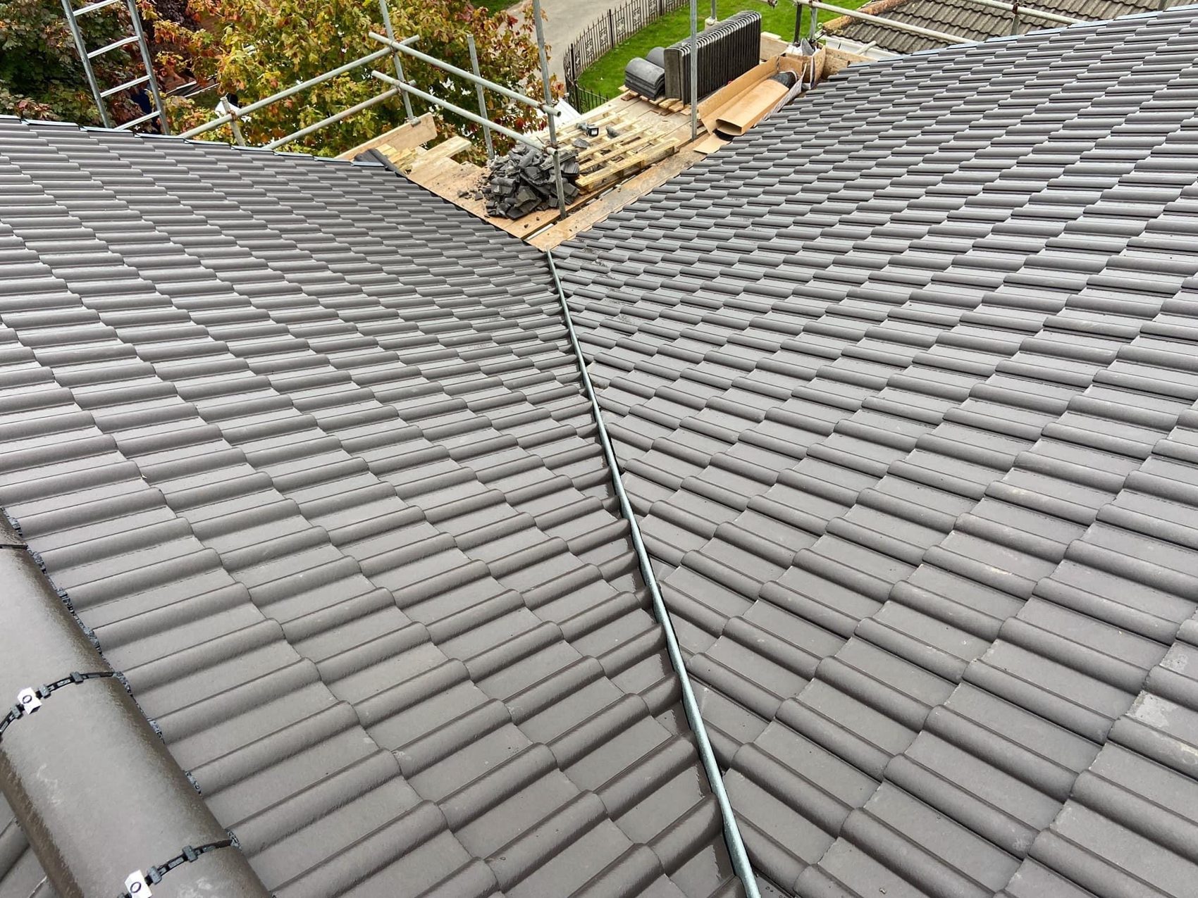 Two new grey tiled roof slopes meeting at a ridge, with scaffold behind