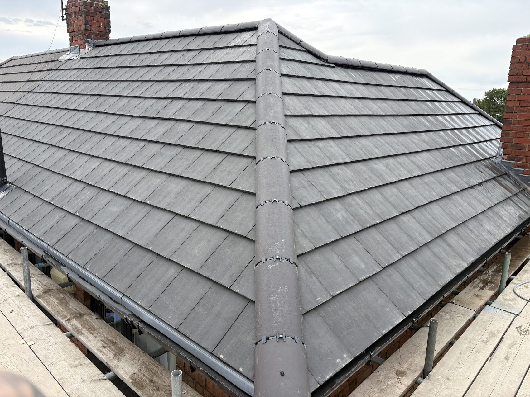A new grey tiled hip roof with a neat ridge and scaffold along the edge