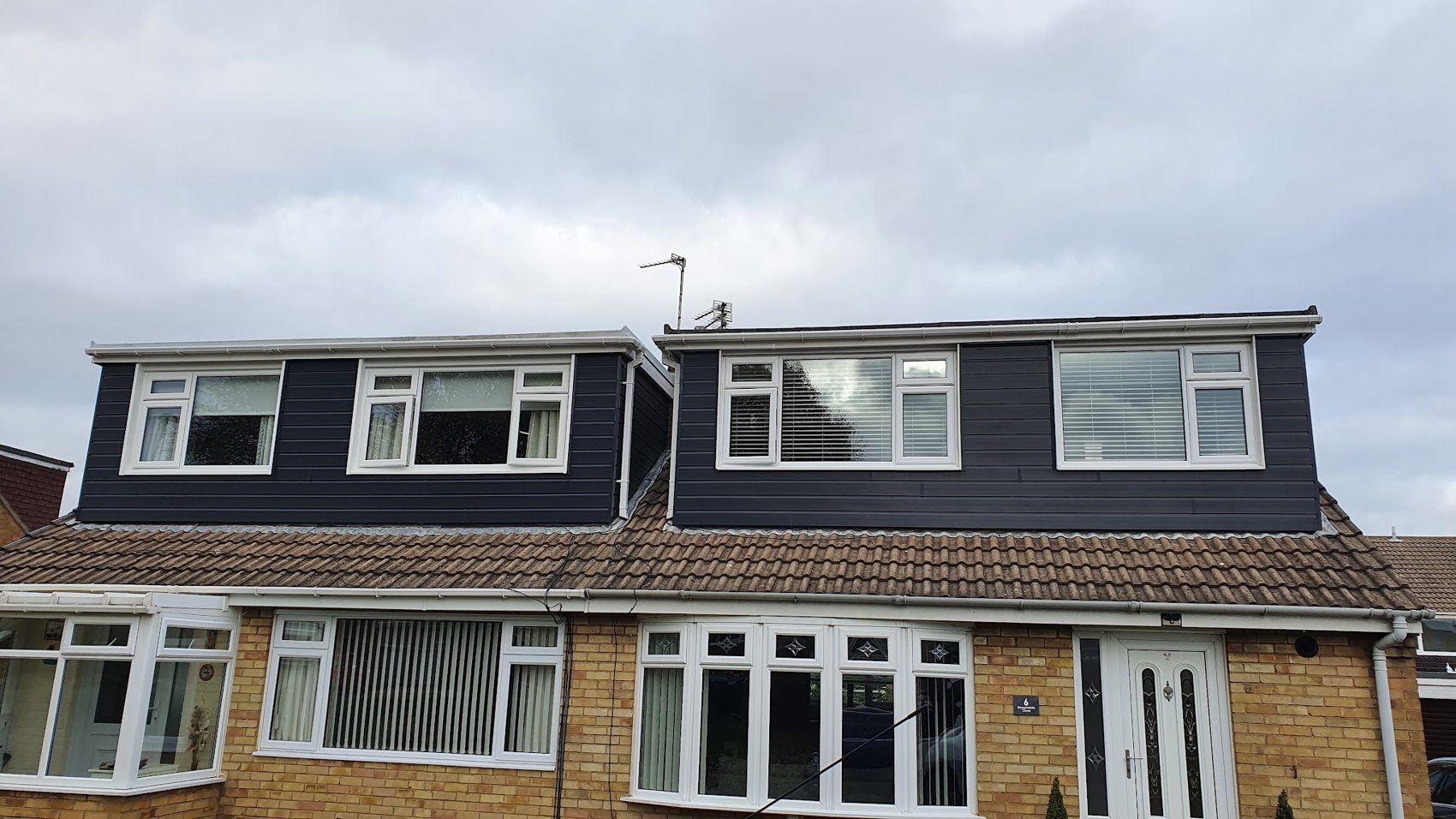 A dormer with dark cladding and new white windows above a brick house